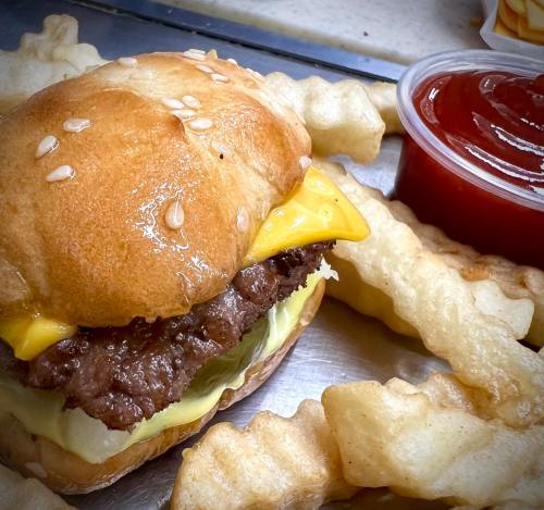 A close-up of a cheeseburger with lettuce on a sesame seed bun, accompanied by crispy fries and a cup of ketchup.