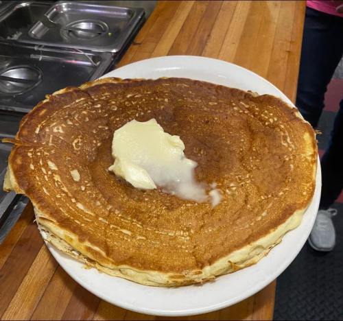 A large, golden-brown pancake topped with a pat of melting butter on a white plate.
