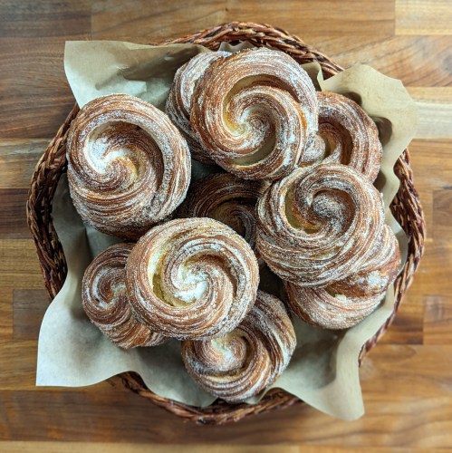 A basket filled with spiral-shaped pastries, dusted with flour, resting on parchment paper.