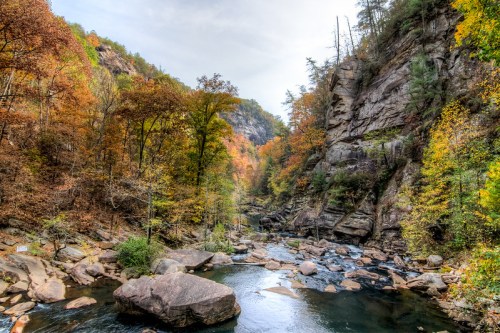 A serene river flows through a colorful autumn landscape with rocky cliffs and vibrant foliage.