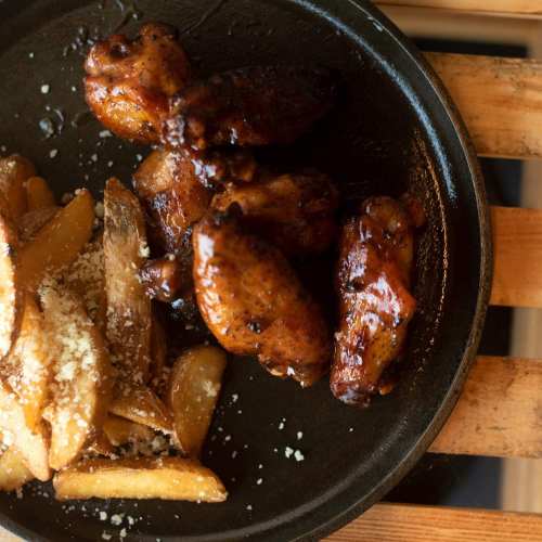 A plate of glazed chicken wings served with crispy potato wedges, garnished with cheese.