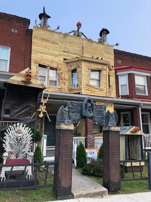 A spooky Halloween-themed house with skeletons, witches, and wooden decorations on the roof and front yard.