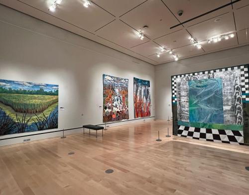 Art gallery interior featuring colorful paintings on the walls and a patterned installation in the center.