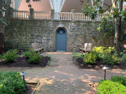 A serene garden path leads to a stone wall with a blue door, flanked by benches and lush greenery.