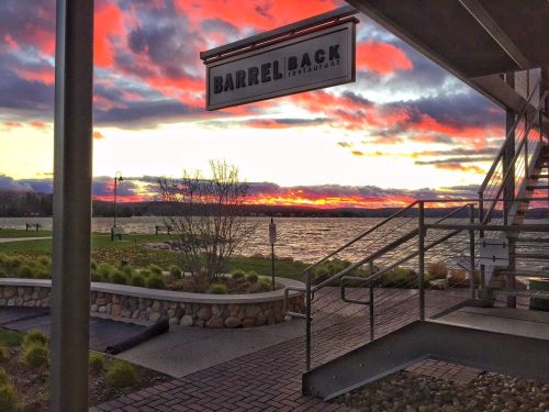A vibrant sunset over a lake, viewed from the entrance of Barrel Back restaurant, with clouds in shades of orange and purple.