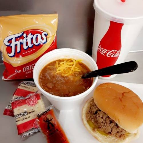 A meal featuring a burger, chili with cheese, Fritos, saltines, and a Coca-Cola drink.