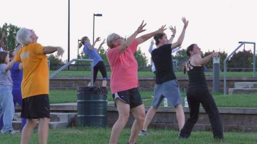 A group of people of various ages participating in an outdoor exercise class, stretching and moving energetically.