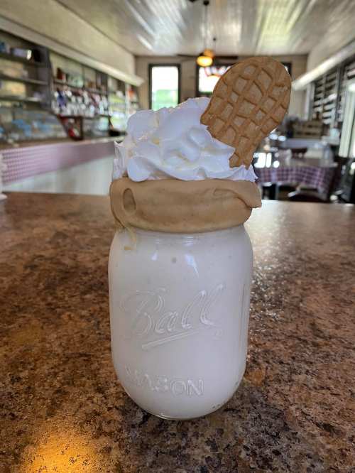 A mason jar filled with a creamy milkshake topped with whipped cream and a cookie, set on a rustic countertop.