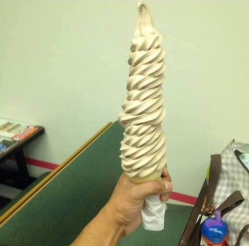 A hand holding a large, swirled soft serve ice cream cone with a chocolate and vanilla mix.