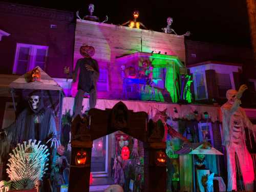 A spooky Halloween display featuring skeletons, a pumpkin, and eerie lighting on a house facade.