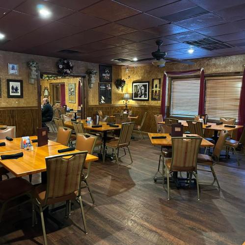 Cozy restaurant interior with wooden tables, chairs, and warm lighting; a few patrons seated in a relaxed atmosphere.
