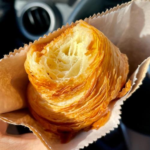 A flaky, golden-brown croissant held in a paper bag, showcasing its airy layers and buttery texture.