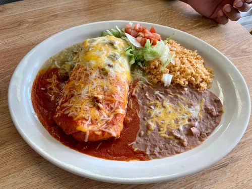 A plate of enchiladas topped with cheese and sauce, served with rice, refried beans, lettuce, and diced tomatoes.