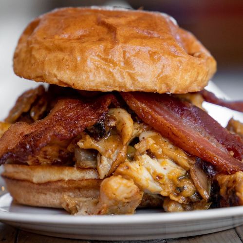 A close-up of a sandwich with crispy bacon and shredded chicken on a toasted bun, served on a plate.