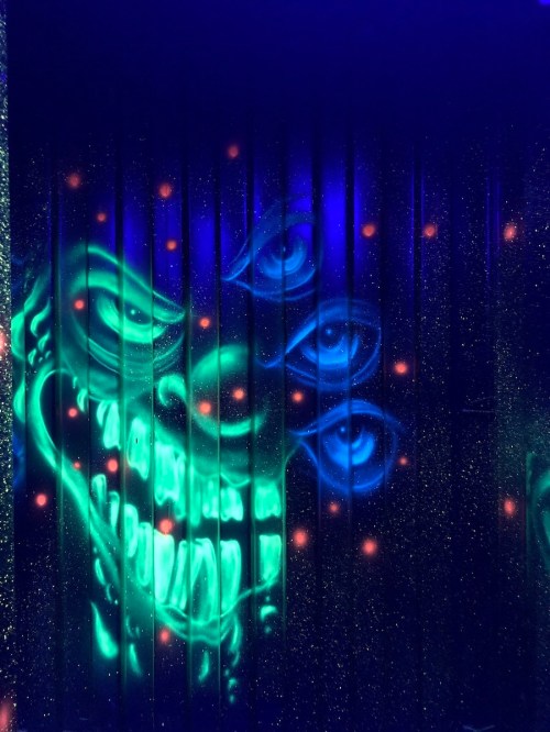 A vibrant mural featuring a grinning skull with multiple eyes, set against a dark, starry background.