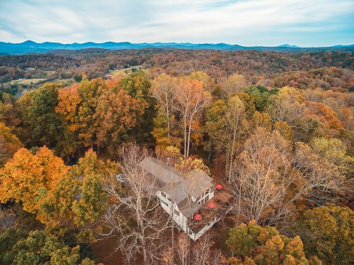 Aerial view of a house surrounded by vibrant autumn trees and mountains in the background.