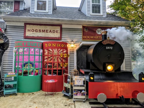 A whimsical storefront resembling Hogsmeade, featuring a train and colorful shop windows for sweets and magical items.
