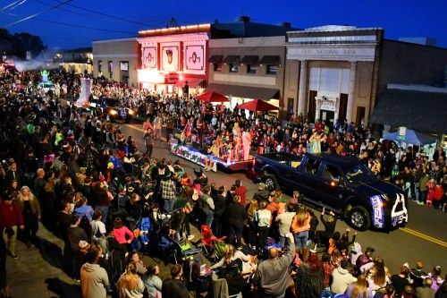 A lively parade at night with colorful floats and a large crowd enjoying the festivities on a bustling street.