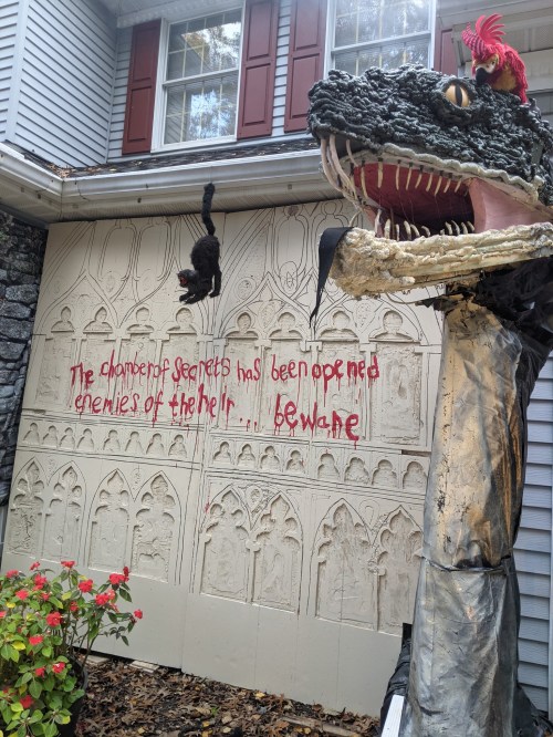 A spooky Halloween display featuring a dragon head, a hanging cat, and a wall with eerie text warning of secrets.