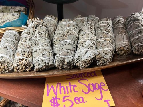 Bundles of white sage tied with string, displayed on a tray with a sign indicating the price of $5 each.