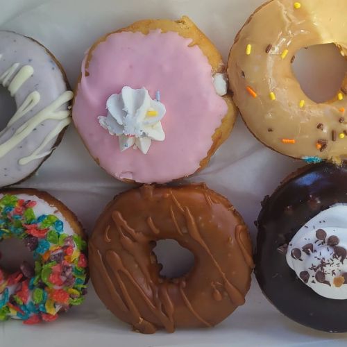 A variety of colorful donuts with different toppings, including sprinkles, frosting, and chocolate drizzle, arranged in a box.