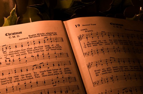Open sheet music for "Christmas" with lyrics and notes, illuminated by soft candlelight and surrounded by greenery.