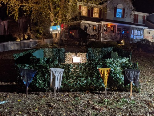 A spooky Halloween display with banners and a maze of ivy in front of a decorated house at night.