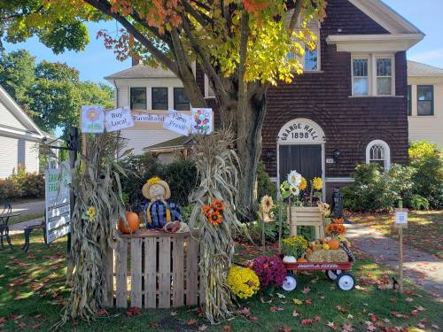 A festive autumn display with a scarecrow, pumpkins, and flowers in front of a charming house.