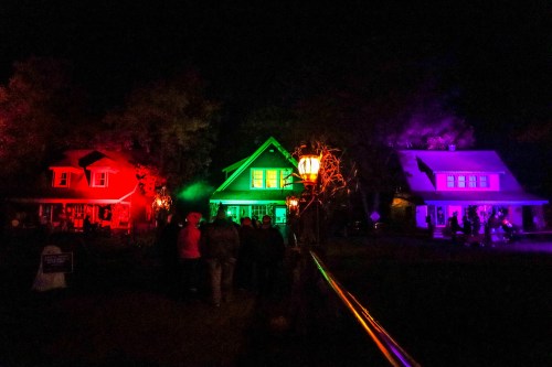 Colorful houses illuminated in red, green, and purple lights at night, with people walking along a path.