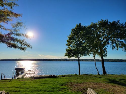A serene lake scene with sunlight reflecting on the water, framed by trees and a grassy shore.