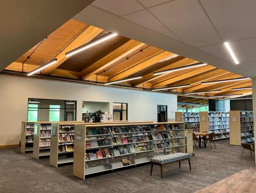 A modern library interior featuring wooden beams, shelves of books, and a cozy seating area.