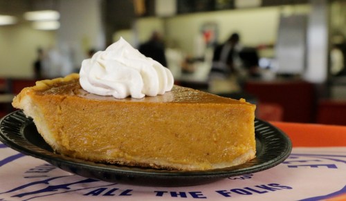A slice of pumpkin pie topped with whipped cream on a black plate, set against a blurred background.