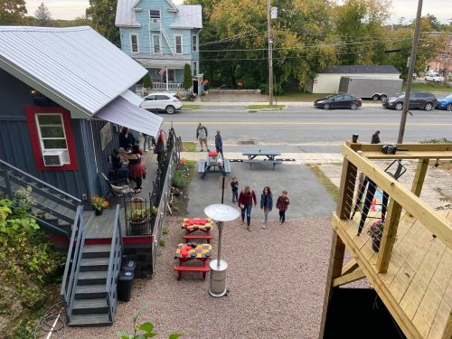 A view from above of a small gathering outside a building, with people walking and tables set up in a gravel area.