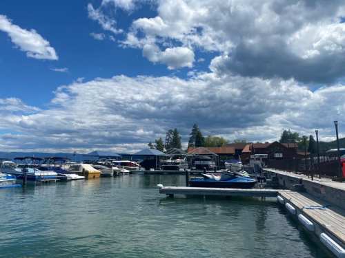 A scenic marina with boats docked, under a partly cloudy sky and surrounded by trees and buildings.