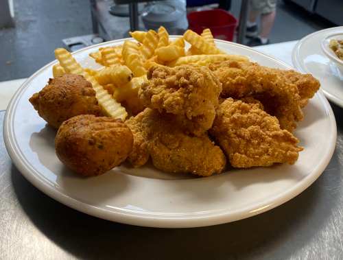 A plate of crispy fried chicken pieces, crinkle-cut fries, and two golden hushpuppies.