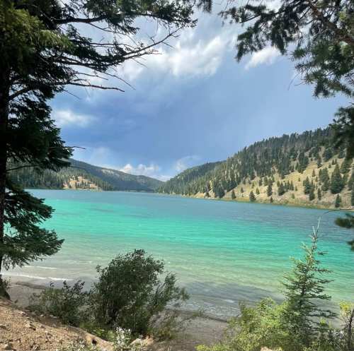 A serene lake surrounded by lush green trees and mountains under a partly cloudy sky.