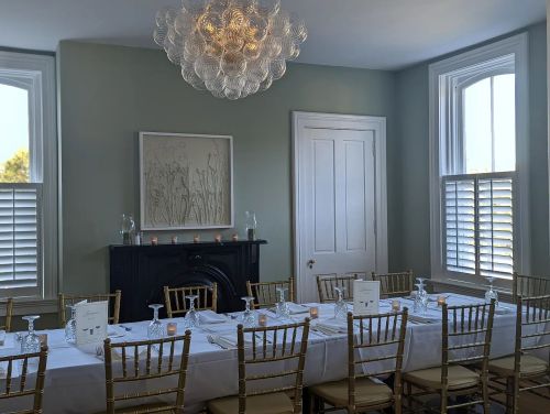 Elegant dining room with a long table set for a meal, featuring a modern chandelier and soft green walls.
