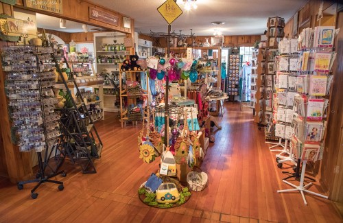 A cozy gift shop interior with wooden floors, displaying various items on shelves and a colorful hanging display in the center.