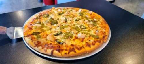A freshly baked pizza topped with cheese, jalapeños, and chicken on a black table.
