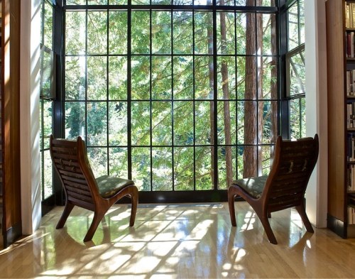 Two wooden chairs facing a large window with a view of lush greenery and sunlight streaming in.