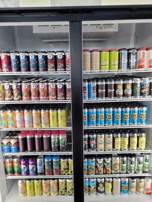 A refrigerator filled with various colorful beer cans arranged neatly on shelves.