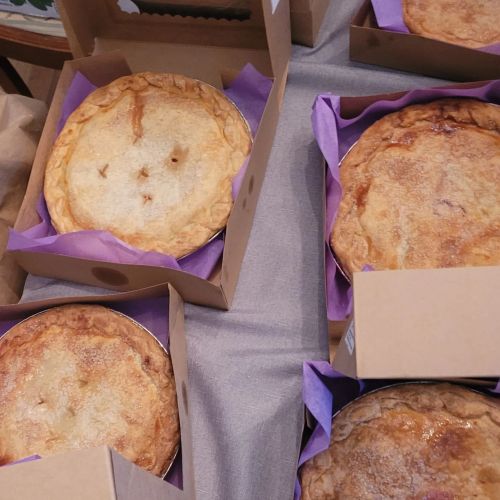 Several freshly baked pies in cardboard boxes with purple liners, arranged on a table.