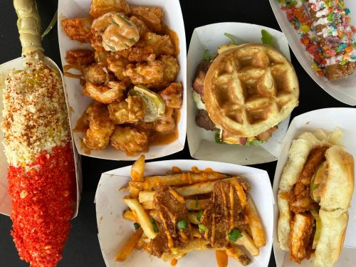 A variety of food items including a waffle sandwich, fried shrimp, loaded fries, and a colorful corn on the cob.