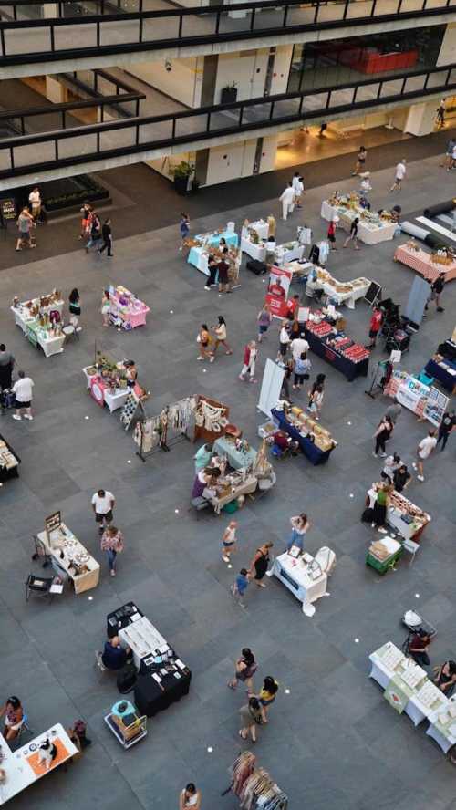 Aerial view of a bustling market with various vendor tables and people shopping in a spacious indoor area.