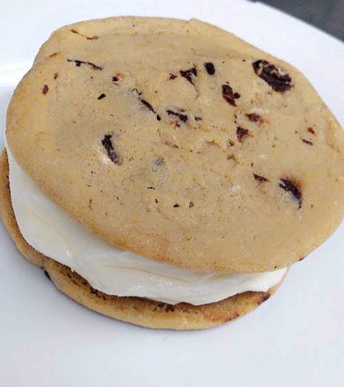 A chocolate chip cookie sandwich filled with creamy vanilla ice cream, placed on a white plate.