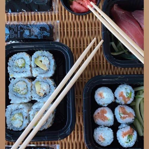 A variety of sushi rolls arranged in black containers with chopsticks on a woven mat.