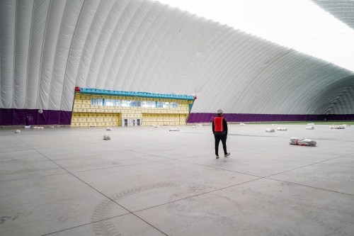 A person walks through a large, empty indoor space with a high, curved ceiling and colorful wall sections.