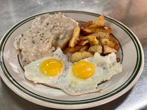 A plate of breakfast featuring two sunny-side-up eggs, seasoned potatoes, and creamy sausage gravy over biscuits.