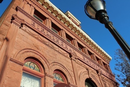 Historic brick building with ornate details and a streetlamp in the foreground against a clear blue sky.