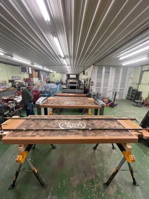 A workshop with wooden tables in progress, featuring a "Mack" logo, surrounded by tools and equipment.